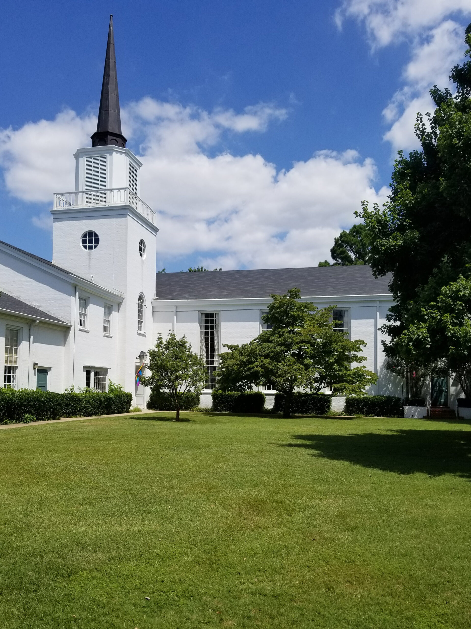 An image of All Souls Unitarian Church in Tulsa, Oklahoma, taken from Peoria Avenue. A classic, New England style church with a striking white exterior inhabits a vast, green campus.