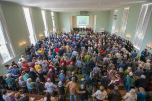 A large group of people standing and holding hands inside a bright, spacious church sanctuary.