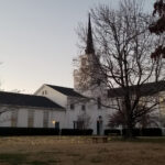 A view across a lawn of a large white church in winter, with a large tree barren of leaves in the foreground.