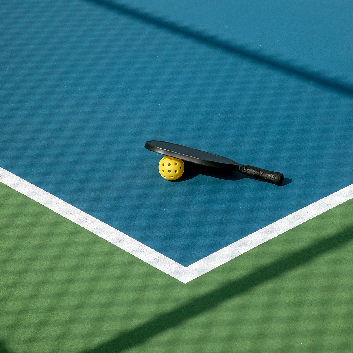 A pickleball paddle and yellow ball resting on a blue and green court.