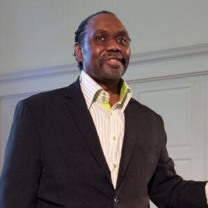 David B. Smith smiling, wearing a button-down shirt, standing in the Sanctuary at All Souls Unitarian Church.