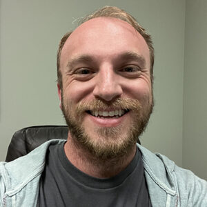 Garrett Powders smiling, wearing a light gray hoodie, with an office background.