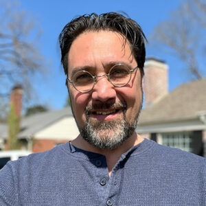 Jerry Burleson smiling, with dark hair and a beard, wearing a dark sweater outside.