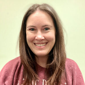 Kacy Selby smiling, with long brown hair, in a warmly lit room.