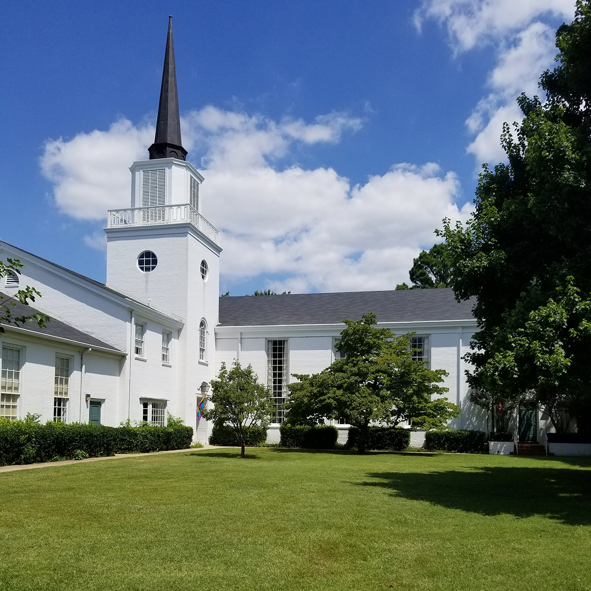 An image of All Souls Unitarian Church in Tulsa, Oklahoma, taken from Peoria Avenue. A classic, New England style church with a striking white exterior inhabits a vast, green campus.