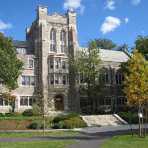 Harvard Divinity School's Andover Hall, a historic stone building with Gothic architecture, surrounded by trees and greenery.