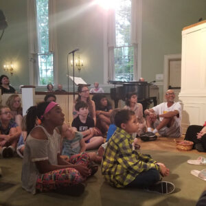 Children and adults sitting on the floor during a Sunday service at All Souls Unitarian Church.