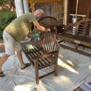 A church volunteer refinishing a wooden bench outside as part of a maintenance project.