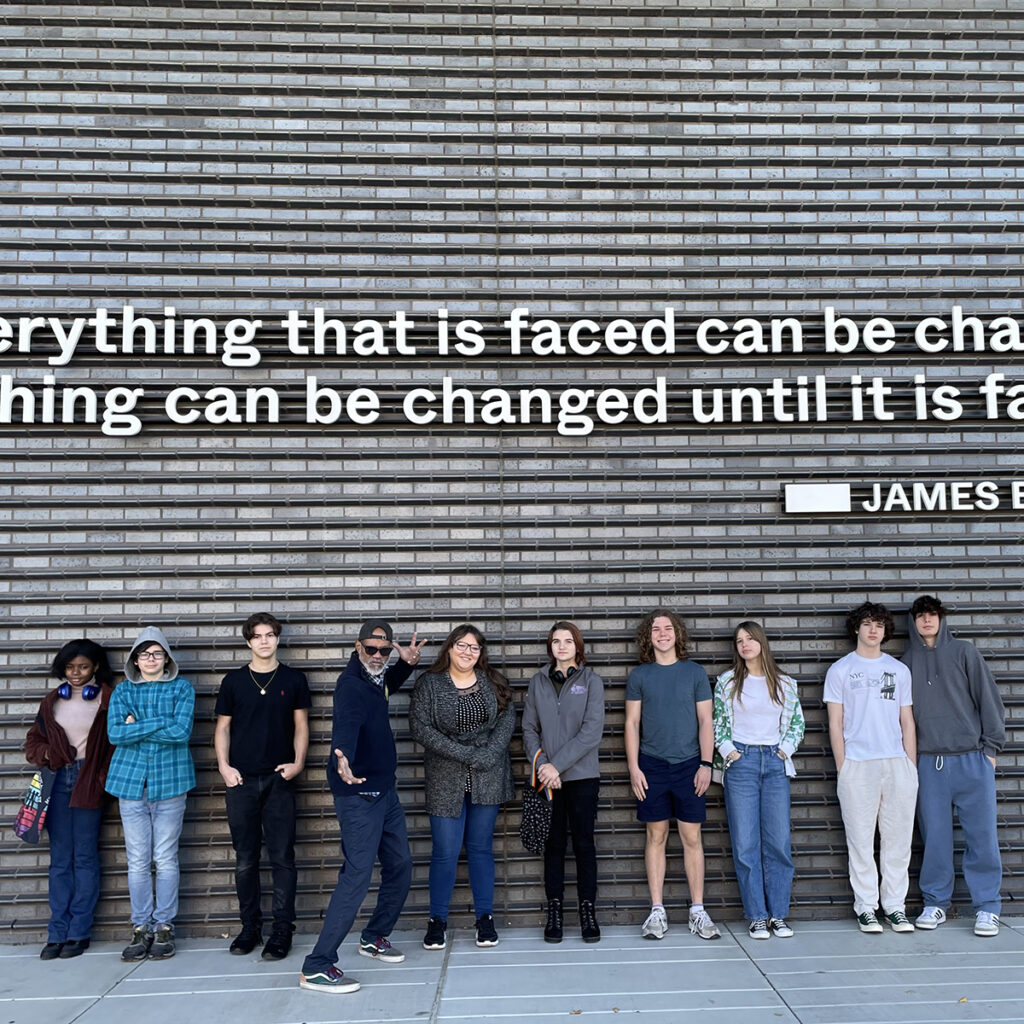 A group of Coming of Age youth and leaders stand in front of a wall with a James Baldwin quote.