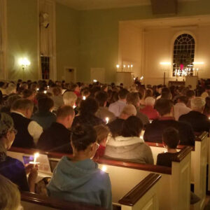 A crowded sanctuary lit by candlelight during a Christmas Eve service at All Souls Unitarian Church.