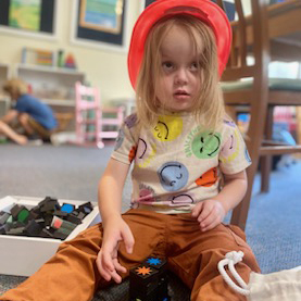 A young child wearing a bright outfit plays with toys in the family room.
