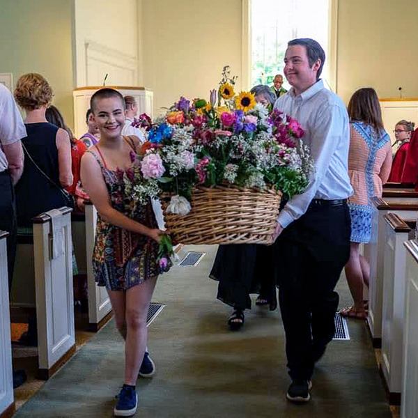 Two people carrying a large basket of flowers down the aisle for the Flower Communion service at All Souls Unitarian Church.