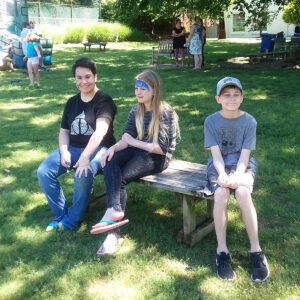 Children enjoy the outdoors during a 2019 event, sitting together and smiling on a sunny day.