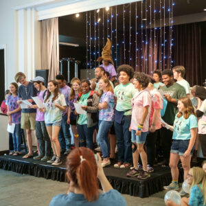 Youth stand on stage, smiling and singing, as part of All Souls Summer Camp.