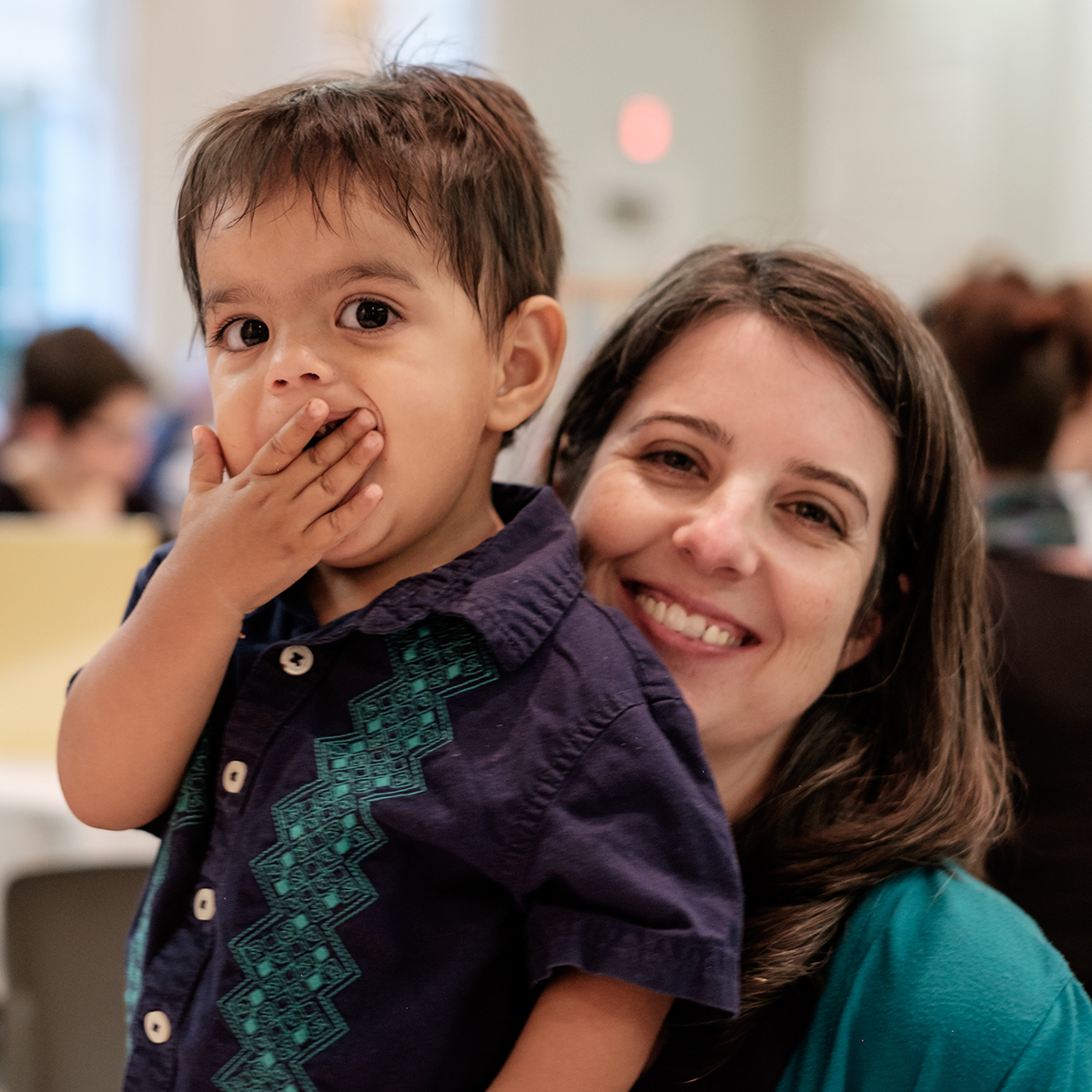 A woman and child share a moment together, the child covering their mouth playfully, during an All Souls community gathering.