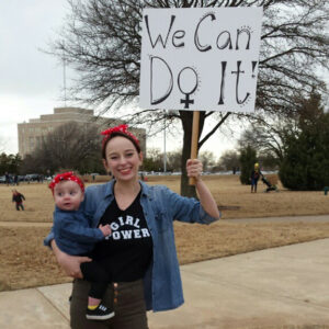 A mother and child, dressed in matching outfits, hold a 'We Can Do It!' sign at the 2017 Women's March.