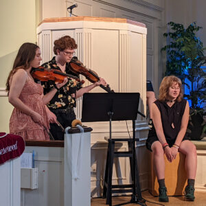 Two youth playing violins and one on a percussion box perform together during a service at All Souls Unitarian Church.