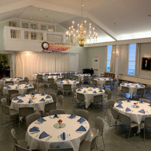 A spacious meeting hall filled with round tables set with blue and white linens.