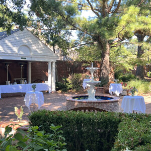 A walled garden with a small pavilion and fountain, set up with small tables with white linens.