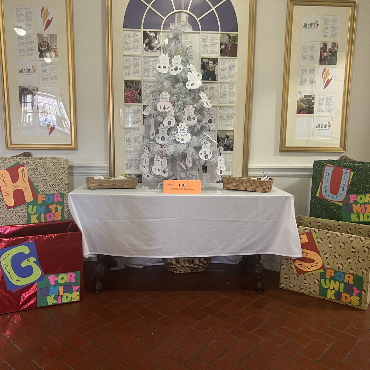 The All Souls HUGS tree, a silver tinsel Christmas tree hung with snowman tags and surrounded by gifts.