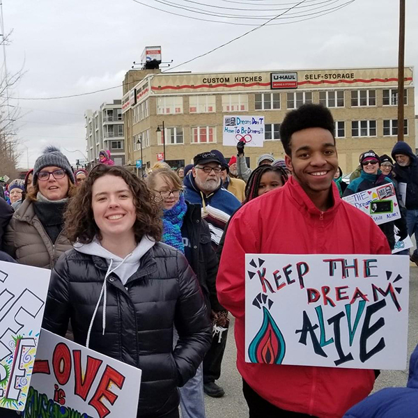 Smiling marchers in coats and hats hold signs saying, 'Be the Change' and 'Keep the Dream Alive' during a the MLK Parade.