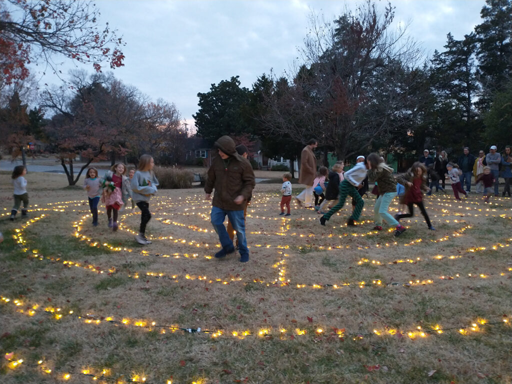 A group of kids running around a labyrinth made of Christmas lights laid on the ground.