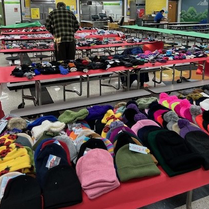 Tables in a school cafeteria are piled with warm winter hats and gloves.